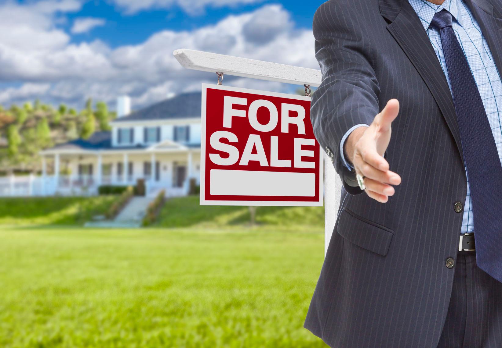 42847518 - real estate agent reaches for handshake with sale sign and new house behind.