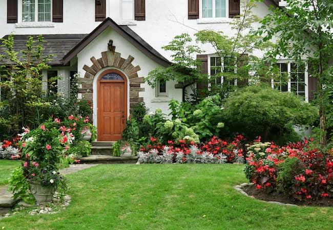 Stucco house with red flowers in the front yard.